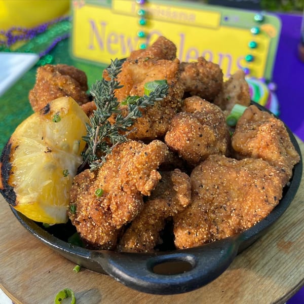 Crispy fried chicken bites with herbs and a grilled lemon wedge in a cast iron skillet.