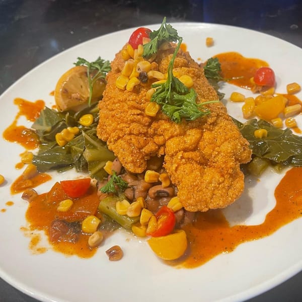 Crispy fried fish with corn, tomatoes, collard greens, and black-eyed peas in a red sauce.