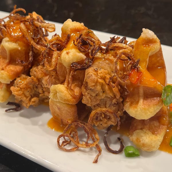 Crispy fried chicken and waffles drizzled with orange sauce and topped with fried onions.